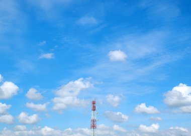 Güneşli bir günde kabarık beyaz bulutlarla dolu canlı mavi gökyüzüne karşı dimdik duran bir telekomünikasyon kulesi..