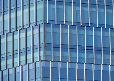 Şehir ortamında yansıtıcı pencereler ve geometrik desenler içeren modern cam ofis ön cephesine yakın plan.