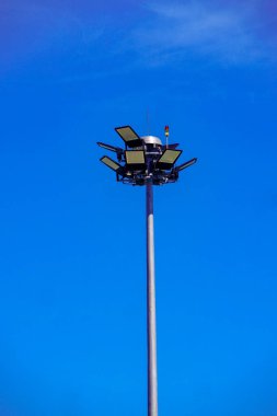 Açık mavi gökyüzüne karşı birden fazla ışığı olan uzun bir sokak lambası, güneşli bir günde yakalanır..