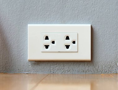 Modern bir elektrik prizinin, ahşap zeminli gri bir duvara monte edilmiş yakın plan görüntüsü, çağdaş ev tasarımı sergileniyor..