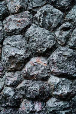 Gri tonlarda doğal kaya desenlerini ve dokularını gösteren sert taştan bir duvarın ayrıntılı görüntüsü..