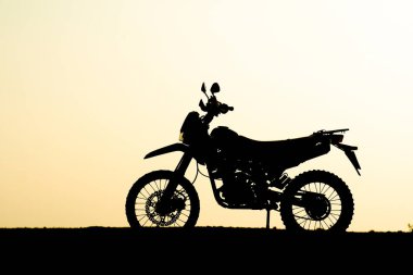 Bir motosikletin çarpıcı silueti, altın bir günbatımı gökyüzüne karşı çöl manzarasının engebeli güzelliğini vurguluyor..