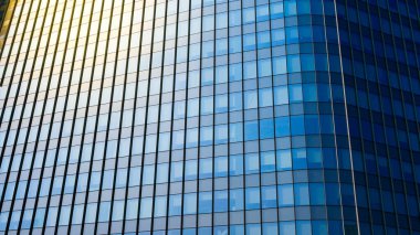 Yansıtıcı pencereleri olan, kentsel iş bölgesinde güneş ışığını yakalayan modern bir cam gökdelenin yakın çekimi..