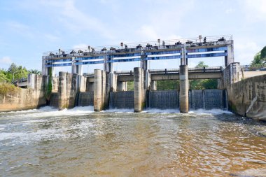 Güneşli bir günde, açık mavi gökyüzüne karşı akan, kapılardan akan büyük bir sanayi barajı..