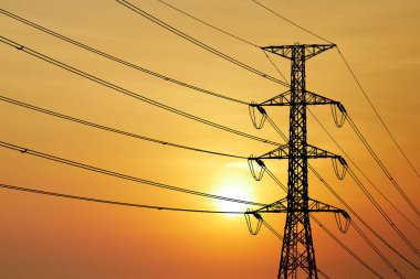 Yüksek voltajlı elektrik hatlarının silueti ve canlı turuncu günbatımı gökyüzüne karşı kule enerji ve altyapının özünü yakalıyor..