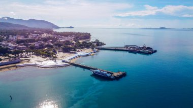 Bir rıhtım, dağlar ve açık mavi gökyüzünün yer aldığı muhteşem bir kıyı kasabası manzarası. Seyahat ve doğa teması için mükemmel..
