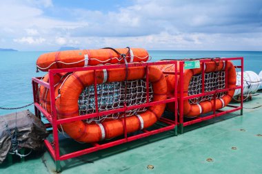 Bir gemi güvertesinde canlı turuncu cankurtaranlar mavi bir okyanus zeminine karşı, deniz güvenliği ve seyahatin altını çiziyor..