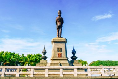 Çarpıcı bir bronz heykel, berrak mavi gökyüzünün altında, sakin bir parkta, yemyeşil bir gökyüzü ile çevrili bir kaidede dimdik duruyor..