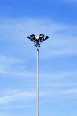 Açık mavi gökyüzüne karşı kurulmuş uzun bir sokak lambası. Şehir altyapısı ve minimalist tasarımı gözler önüne seriyor..