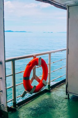 Huzurlu bir feribot yolculuğu berrak turuncu bir can simidi sergiliyor sakin mavi deniz ve uzak adalara karşı.