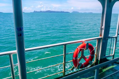 Hayat şamandırası, turkuaz okyanus suları ve açık mavi gökyüzünün altındaki uzak adaları gösteren bir feribot görüntüsü..
