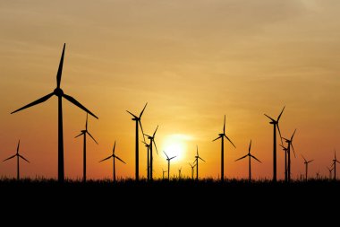 Rüzgar türbinleri, yenilenebilir enerji ve sürdürülebilirliği simgeleyen canlı bir günbatımı gökyüzüne karşı siluetlenmiştir..