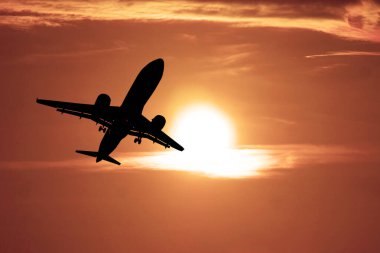 Canlı turuncu bir gün batımına doğru uçan bir uçak siluetinin çarpıcı görüntüsü seyahat ve maceranın özünü yakalıyor..