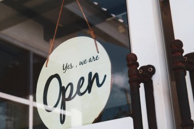 Dükkan kapısında klasik tarzı açık tabela var. Müşterileri içeri buyur ediyor..