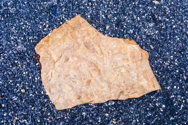 Büyük, dokulu bir taş mavi çakıl yatağında uzanır. Açık havada doğal güzellikler ve kontrastlar sergilerler..