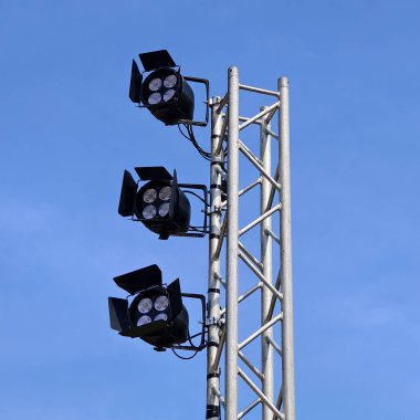 Metal bir direğe monte edilmiş üç stadyum projektörünün yakın plan görüntüsü..