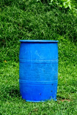 Yeşil bir çim tarlasında duran canlı mavi plastik bir fıçı, açık havada yemyeşil bir yaprakla çevrili..