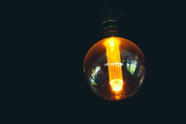 Eskimiş bir Edison ampulünü koyu bir arka planda yakın plan, sıcak ışık ve yansımalar sergiliyor.
