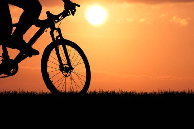 Sersemletici turuncu bir günbatımına karşı bir dağ bisikletinin silueti macera ve özgürlüğün özünü yakalıyor..