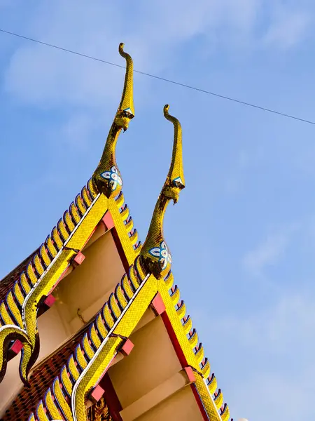 Tayland tapınağındaki karmaşık altın çatı süslemeleri, parlak mavi gökyüzü altında geleneksel mimariyi gözler önüne seriyor..