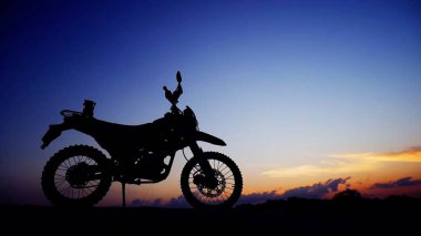 Renkli bir gün batımına karşı çarpıcı bir motosiklet silueti çarpıcı gökyüzünü ve bulutları aydınlatıyor..