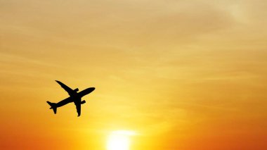 * * Uçak silueti canlı turuncu bir günbatımı gökyüzünde süzülüyor, seyahat ve maceranın özünü yakalıyor.