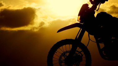 Çarpıcı bir motosiklet silueti dramatik bir günbatımına karşı dizilmiş, canlı renkleri ve gökyüzündeki altın bulutları vurguluyor..