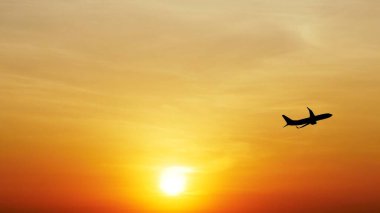 Ufukta güneş batarken canlı turuncu bir günbatımı gökyüzüne doğru uçan bir uçağın silueti..