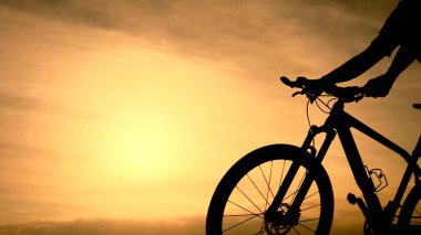 * * Bir bisikletçinin silueti baş döndürücü altın bir gün batımına karşı, sakin doğal bir manzarada macera ve özgürlüğü somutlaştırıyor.