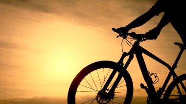 Gün batımında motosikletli bir bisikletçinin silueti açık hava macerasının ve özgürlüğün özünü yakalıyor..