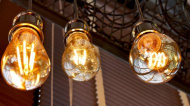 Tavandan sarkan parlayan klasik Edison ampullerinin yakın çekimi endüstriyel bir dokunuşla sıcak ve davetkar bir atmosfer yaratıyor..