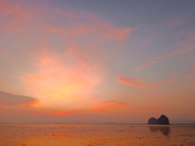 Sakin okyanus sularına yansıyan canlı renklerle büyüleyici günbatımı sahnesi, uzak ada siluetlerini aydınlatıyor..