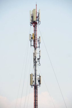 Açık mavi gökyüzüne karşı antenleri olan, modern telekomünikasyon ve kablosuz teknolojiyi simgeleyen yüksek bir iletişim kulesi..