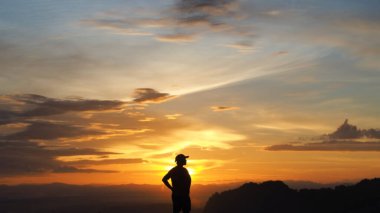 Büyüleyici bir günbatımına karşı silueti olan bir insan, canlı renkler ve gökyüzünde dramatik bulutlar sergiliyor..