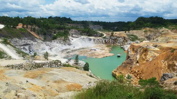 Engebeli arazi ve yemyeşil yemyeşil ile çevrili, çarpıcı bulutlu gökyüzü altında canlı turkuaz suyu içeren terk edilmiş bir taş ocağının havadan çekimi..