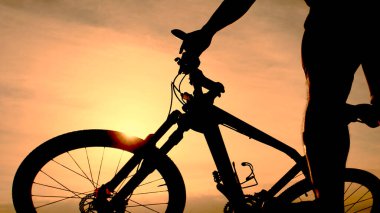 Sersemletici bir gün batımına karşı bisiklete binen bir siluet, açık hava macerası ve özgürlüğün özünü yakalıyor..