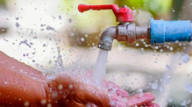 Eller açık bir musluğun altında yıkanır, su damlacıkları gündüz su sıçratır..