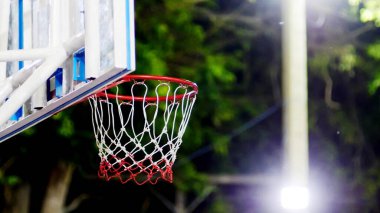Kırmızı kenarlı ve ağlı bir basketbol potasının detaylı bir görüntüsü, parlak ışıklarla aydınlanan, koyu, bulanık bir arka plan.