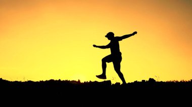 Çarpıcı bir turuncu gün batımına karşı neşeyle zıplayan, özgürlüğün ve maceranın özünü yakalayan dinamik bir siluet..