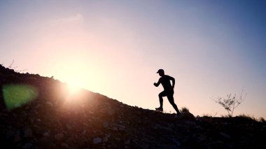 Gün batımı gökyüzüne karşı yokuş yukarı koşan bir insanın silueti, uygunluğu ve kararlılığı simgeliyor..