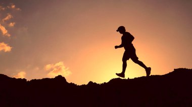 Canlı bir günbatımına karşı silueti olan yalnız bir koşucu tepede zindelik ve kararlılık sergiliyor..