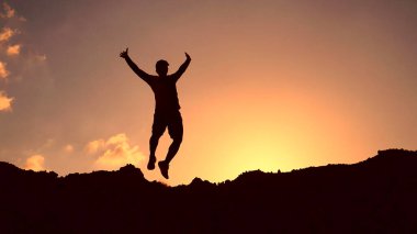 * * Bir insanın silueti çarpıcı bir günbatımına karşı havada sıçrıyor, özgürlük ve neşe dolu bir anı yakalıyor