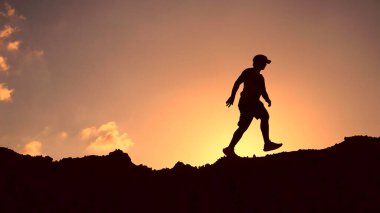 Turuncu gökyüzü ile çarpıcı bir günbatımında dağ sırtında yürüyüş yapan bir insanın silueti..