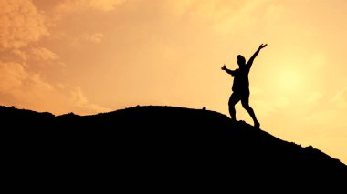 * * Bir tepenin üstünde kollarını kaldırmış bir kişinin silueti, çarpıcı bir günbatımı gökyüzüne karşı kurulmuş.