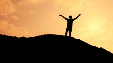 Bir insan zafer dolu bir şekilde bir tepede duruyor, çarpıcı turuncu bir gün batımına karşı silueti var, özgürlüğü ve başarıyı simgeliyor..