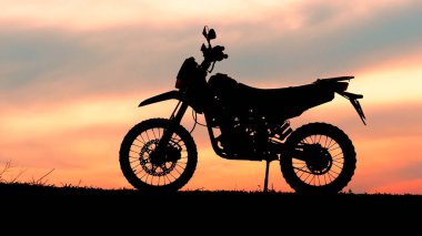 Bir motosiklet silueti rengarenk bir gün batımına karşı duruyor, çarpıcı ve sakin bir açık hava sahnesi yaratıyor..