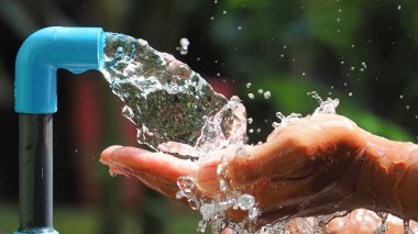 Mavi bir musluktan ellere akan suyun yakın çekimi açık hava ortamında saflığı ve sürdürülebilirliği sembolize ediyor..