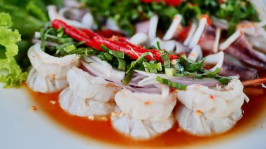 Bitkiler ve sebzelerle süslenmiş taze karides salatası, beyaz bir tabağa baharatlı sos serpiştirilmiş..