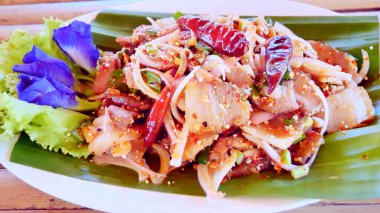 Muz yaprağında servis edilen canlı Tayland domuz salatası taze otlar, kurutulmuş biberler ve renkli bir mutfak sunumu için yenilebilir çiçekler..