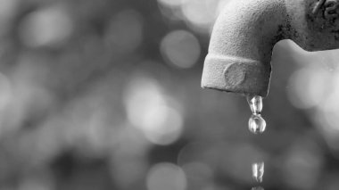 Su musluğunun bulanık arka plan ile damlayan siyah ve beyaz görüntüsü, suyun korunmasını vurguluyor.